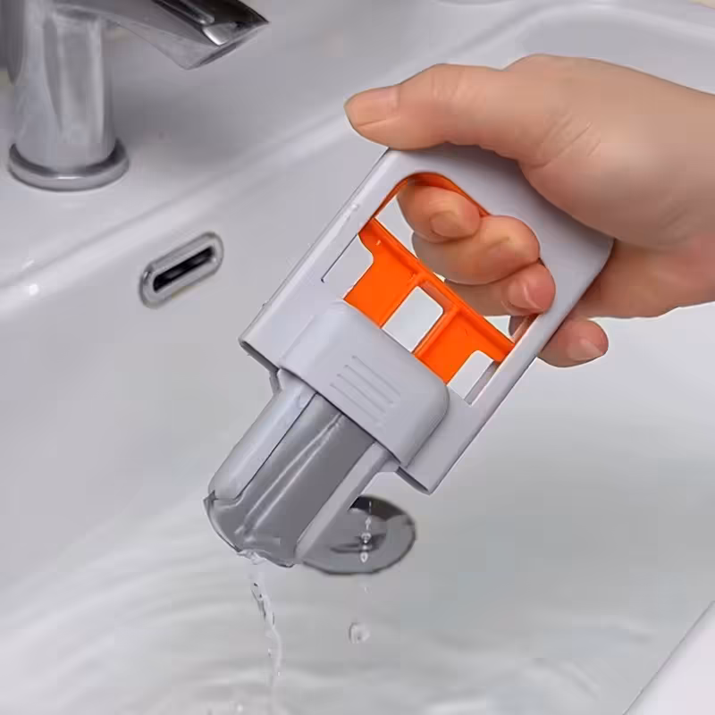 Mão segurando Mini Mop Portátil ao lado de um kit com 3 refis de esponja PVA cinza sobre a mesa.